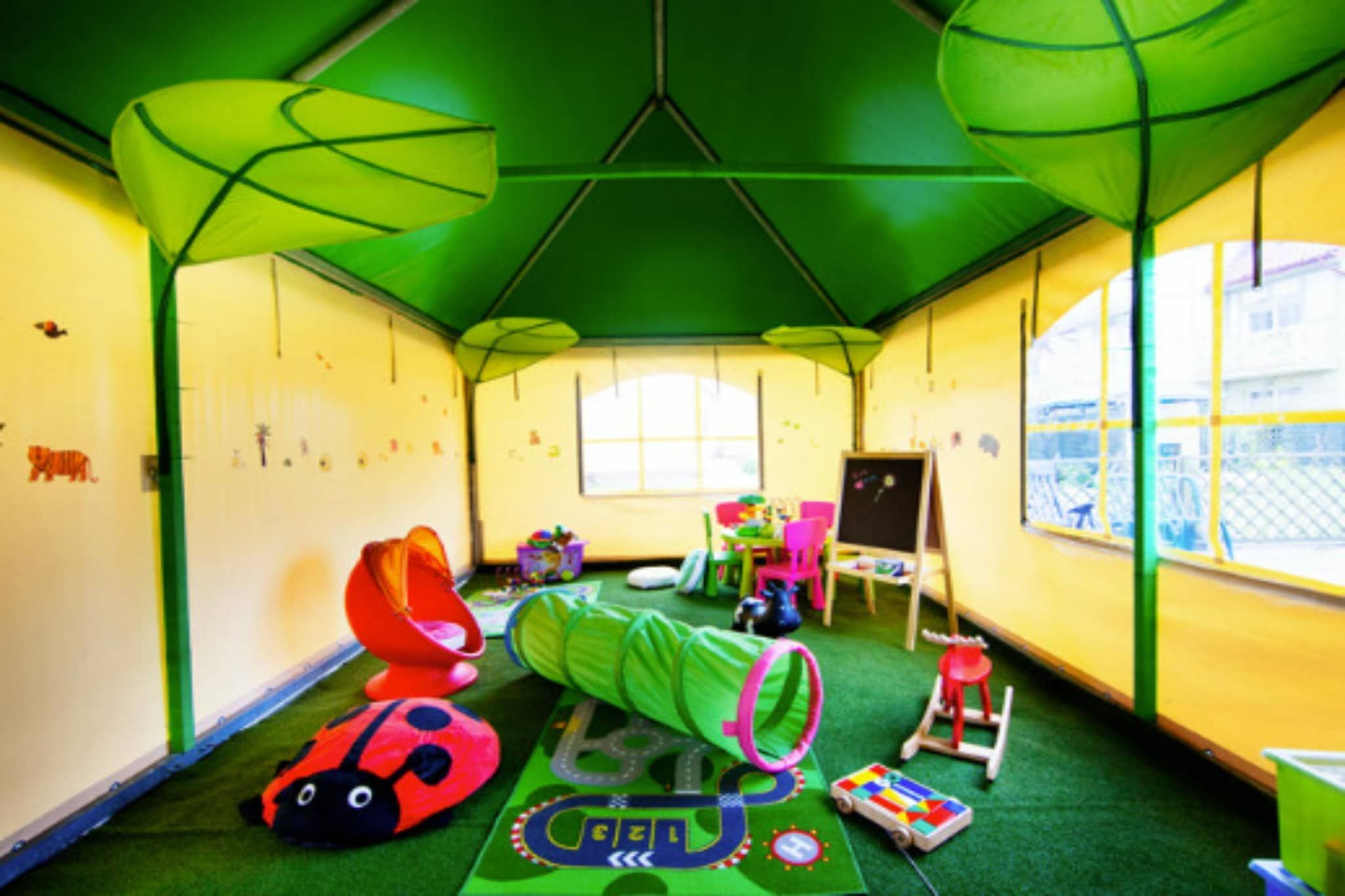 A room with a green ceiling, a large window, a play area with toys, and a green tunnel.