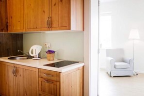 A kitchenette with wooden cabinets, a sink, a kettle, and a small basket with purple flowers. - Large 4-person apartment with a terrace (Debki)