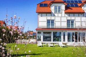 Ein zweistöckiges Haus mit rotem Ziegeldach, großen Fenstern und einer überdachten Terrasse mit Gartenmöbeln.