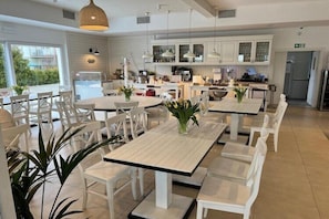 Een moderne keuken met witte kasten, een eethoek met witte tafels en stoelen, en uitzicht op het buitengebied.