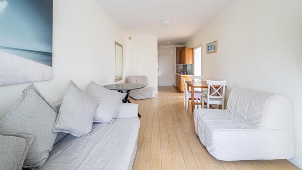 Ein modernes Wohnzimmer mit einer Couch, einem Esstisch mit Stühlen und einer Küche im Hintergrund.
