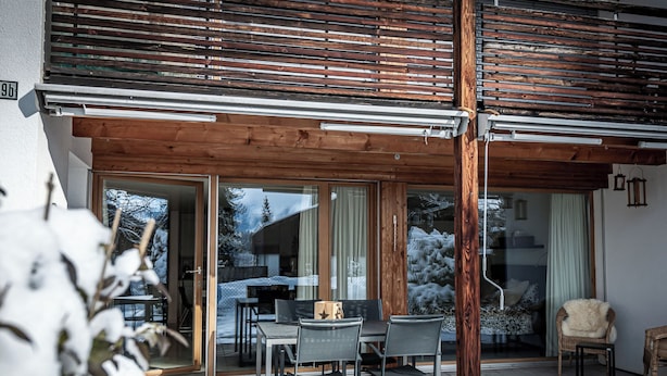 Une terrasse en bois avec une porte vitrée donnant sur un patio abrité.