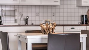 Une cuisine moderne avec des meubles blancs, un luminaire suspendu noir et un porte-bougie en verre orné de branches en bois.