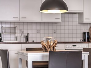 Een moderne keuken met witte kasten, een zwarte hanglamp en een glazen kandelaar met houten takken.