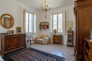 A room with a wooden cabinet, a sofa, a chair, a bookshelf, a mirror, and a chandelier. - A charming, detached, 200-square-meter period house on three levels, accommodating up to 10 people.The property is located in Gravedona e Uniti, a charming village on the northwest shore of Lake Como, known for its historic center and picturesque lakefro (Gravedona ed Uniti)