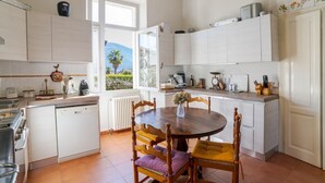 A kitchen with white cabinets, a dining table with chairs, a window with a view, and a radiator. - A charming, detached, 200-square-meter period house on three levels, accommodating up to 10 people.The property is located in Gravedona e Uniti, a charming village on the northwest shore of Lake Como, known for its historic center and picturesque lakefro (Gravedona ed Uniti)