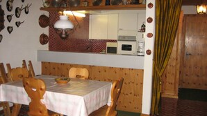 A dining area with a table, chairs, a kitchen in the background, and a patterned floor. - Ner B / Hartl, (Flims Dorf), 29 by Interhome (Flims)