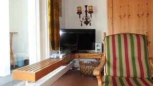 A living room with a television, wooden furniture, a striped chair, and a wooden door. - Ner B / Hartl, (Flims Dorf), 29 by Interhome (Flims)