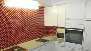 A compact kitchen with a sink, stove, oven, and white cabinets. - Ner B / Hartl, (Flims Dorf), 29 by Interhome (Flims)