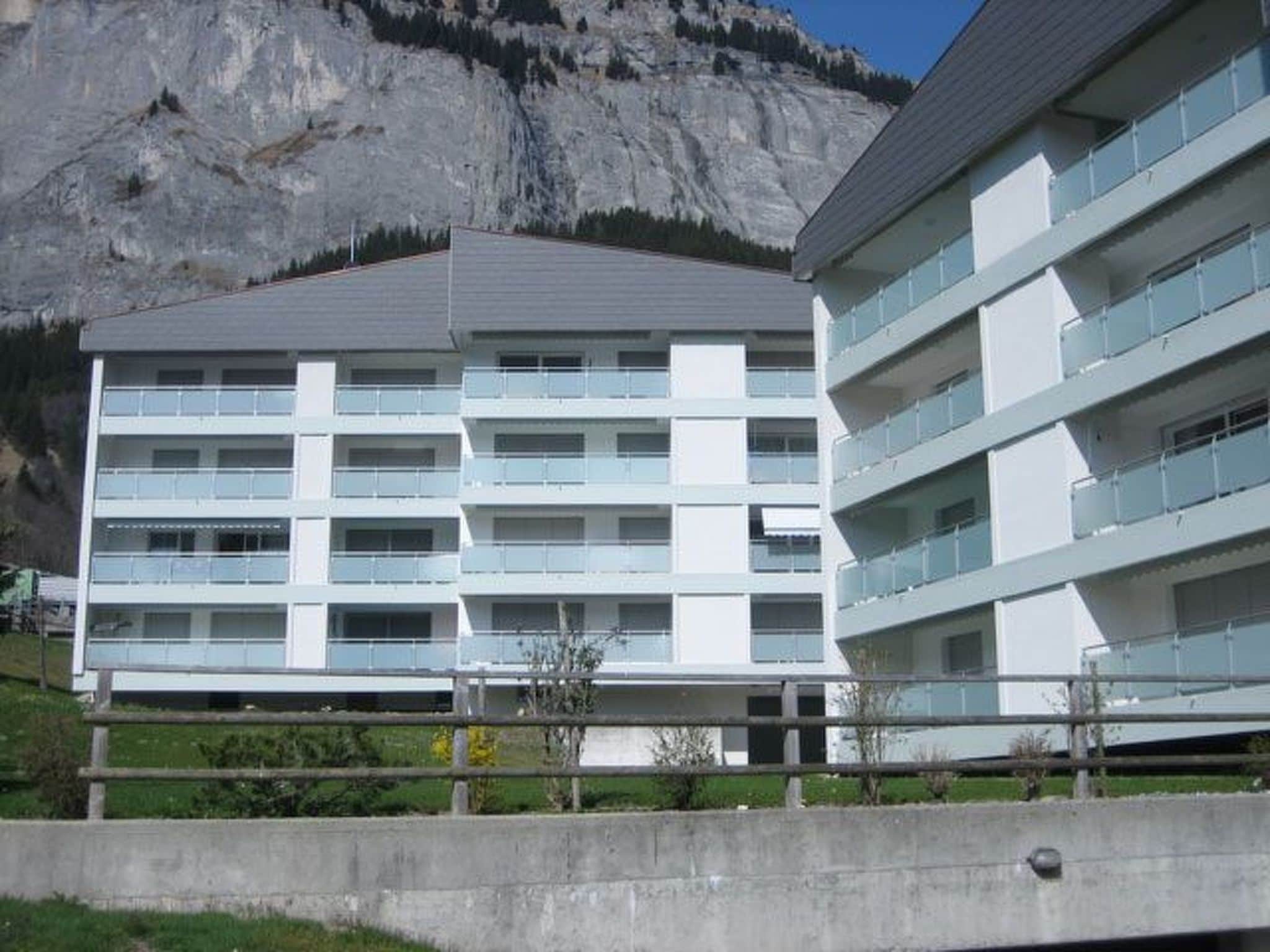 A multi-story building with balconies, set against a mountainous backdrop.