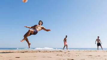 Eine Szene am Strand, mit einer Person, die einen Ball fängt, einer weiteren, die geht, und einer dritten Person im Hintergrund.