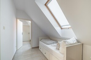 A bedroom with a sloped ceiling, a skylight, a bed with a white mattress and floral pillow, and a white dresser.