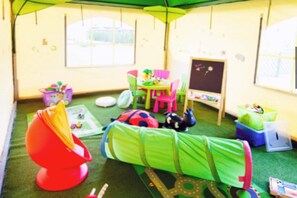 A playroom with a green carpet, a red chair, a green bed, and various toys.