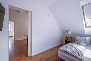 A bedroom with a sloped ceiling, a bed with patterned bedding, a bedside table with a lamp, and a door leading to another room. - Luxury apartment for 6 people, with a bathtub (Debki)