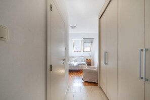 Un couloir étroit mène à une chambre à coucher qui contient un lit, des tables de chevet et une fenêtre.