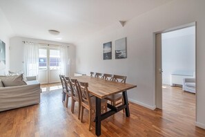 Un vaste espace de vie comprenant une table à manger en bois, un canapé et une vue dégagée sur l’extérieur grâce à une grande fenêtre.