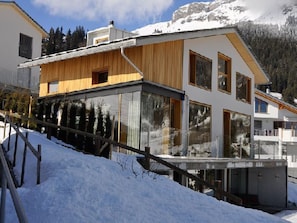 A modern two-story house with large windows and a wooden facade, surrounded by snow and mountains. - Casa Admisa, (Flims Dorf), 2623 by Interhome (Flims)