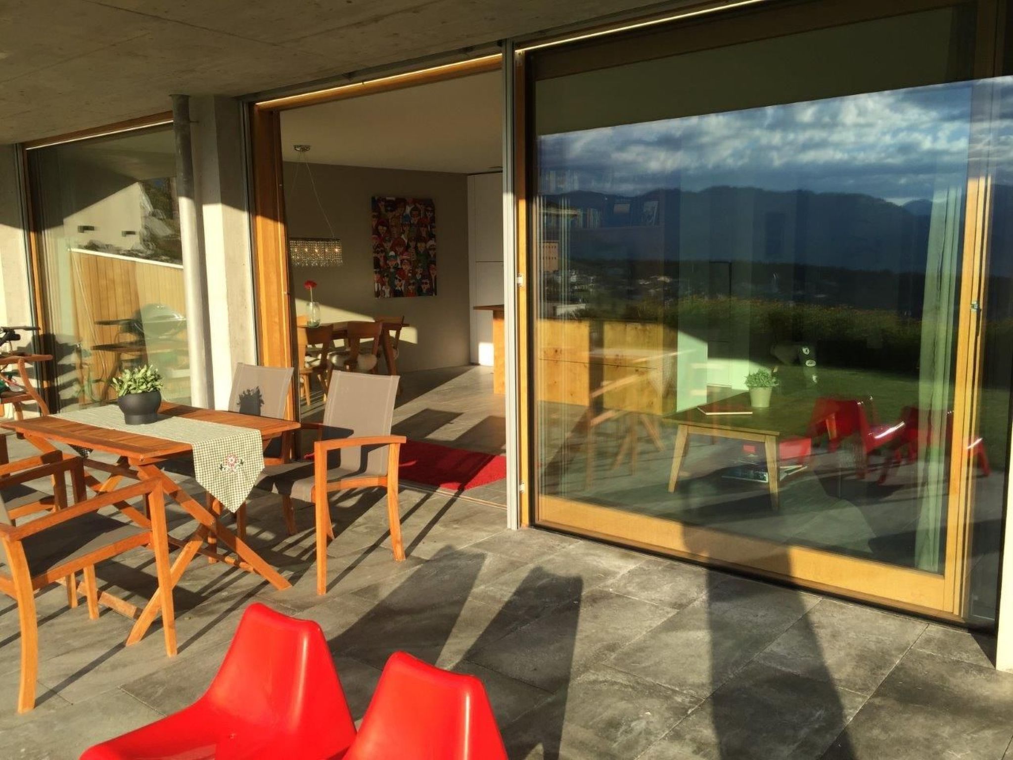 An outdoor seating area with wooden furniture and a glass wall offering a view of the outdoors.