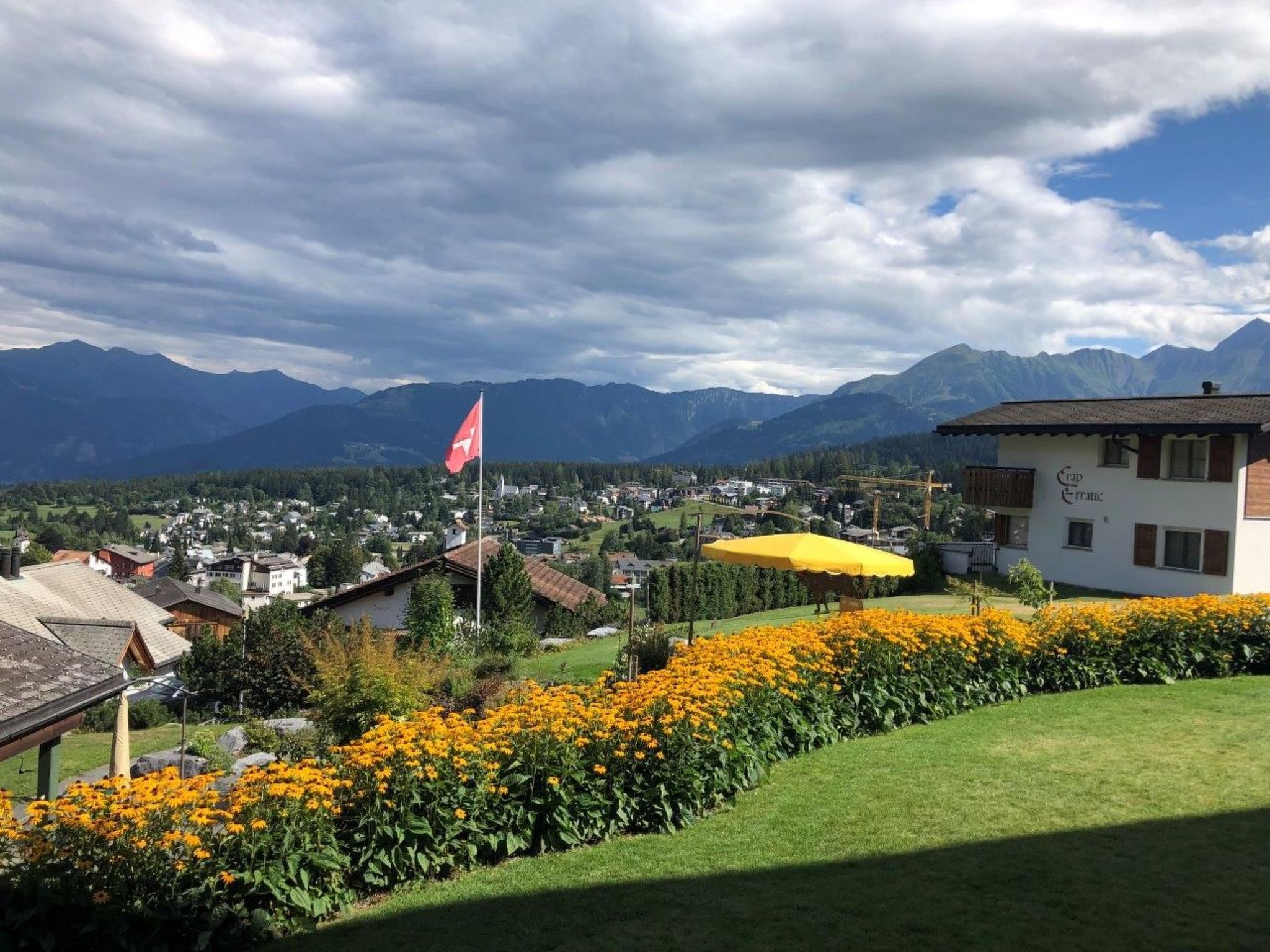 A mountainous landscape with a flag, a building with a yellow awning, and a field of yellow flowers.