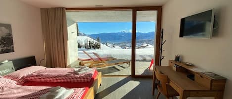 Camera d'albergo con due letti, una scrivania, una sedia, una TV e vista sulle montagne innevate.