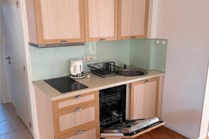 A compact kitchen with wooden cabinets, a countertop, a sink, a kettle, and a dishwasher.