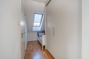 A narrow hallway with wooden flooring leading to a loft bedroom with a skylight.