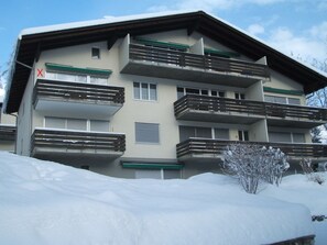 A multi-story building with balconies, a snow-covered ground, and a clear sky. - Casa Guardamunt, (Laax GR), by Interhome (Laax)
