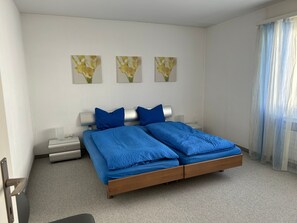 A bedroom with a double bed, two bedside tables, a nightstand, and three wall-mounted flower paintings. - Casa Guardamunt, (Laax GR), by Interhome (Laax)