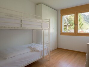 Ein Schlafraum mit Etagenbetten, Holzboden, Fenster mit Blick auf Grünflächen und einem weißen Kleiderschrank.