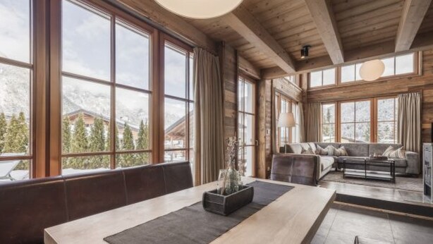 A spacious room with large windows, a wooden ceiling, and a seating area with a sofa and a table.