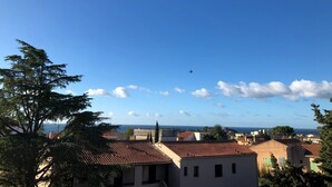 A coastal town with terracotta-roofed buildings, a clear blue sky, and a distant airplane. - Sea view apartment, quiet residence, 10 minutes from the center and beaches. (Bandol)