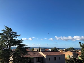 Eine Küstenstadt mit terrakottafarbenen Dächern, blauem Himmel und einem entfernten Flugzeug.