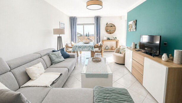 A modern living room with a sofa, coffee table, TV, and a dining area with chairs and a table. - Sea view apartment, quiet residence, 10 minutes from the center and beaches. (Bandol)