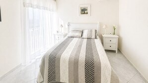 A bedroom with a bed, two bedside tables, a hanging lamp, a picture on the wall, and an air conditioning unit. - Sea view apartment, quiet residence, 10 minutes from the center and beaches. (Bandol)