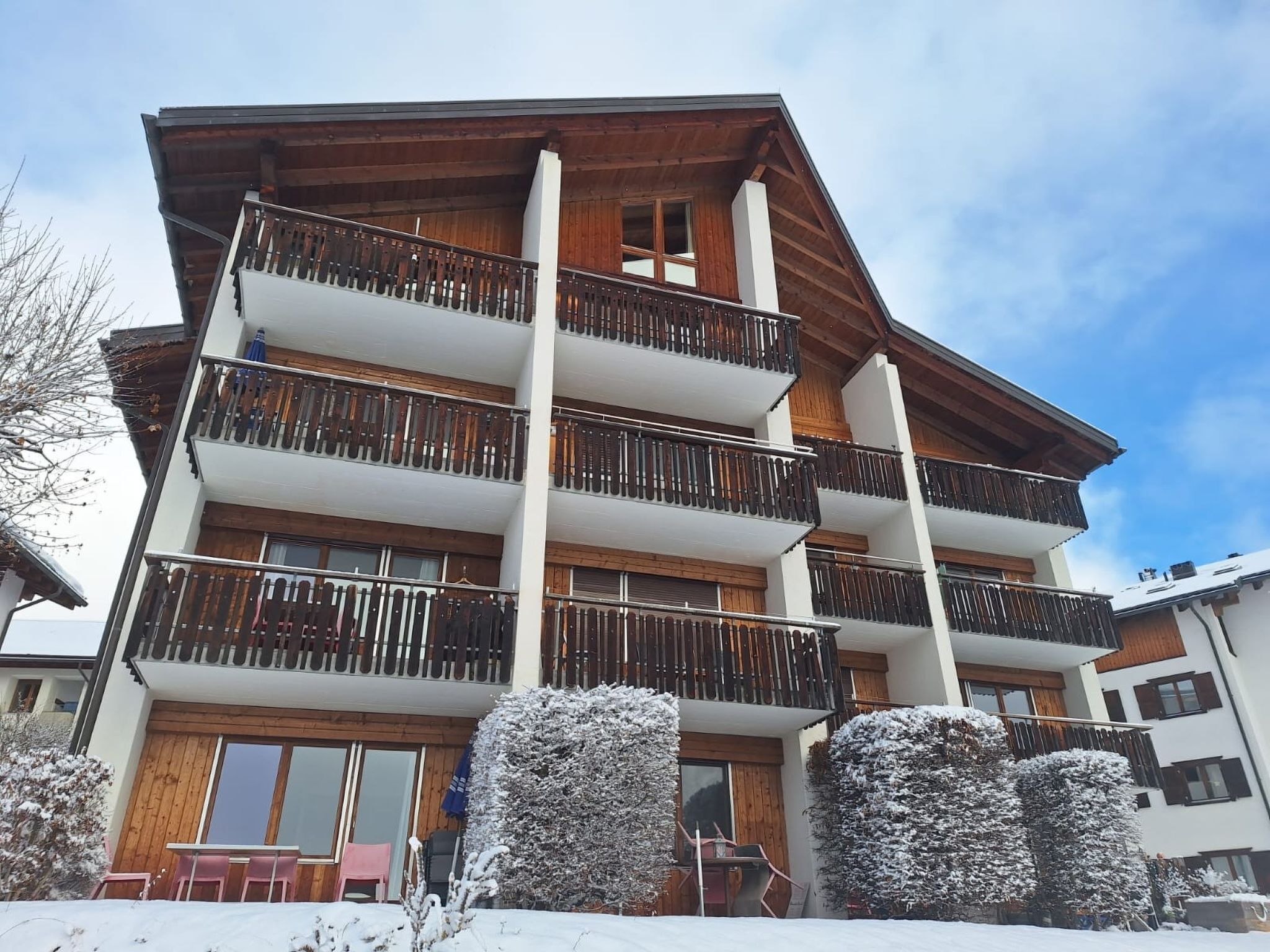 Un immeuble à plusieurs étages doté de balcons, d’une façade en bois et entouré d’un paysage enneigé.