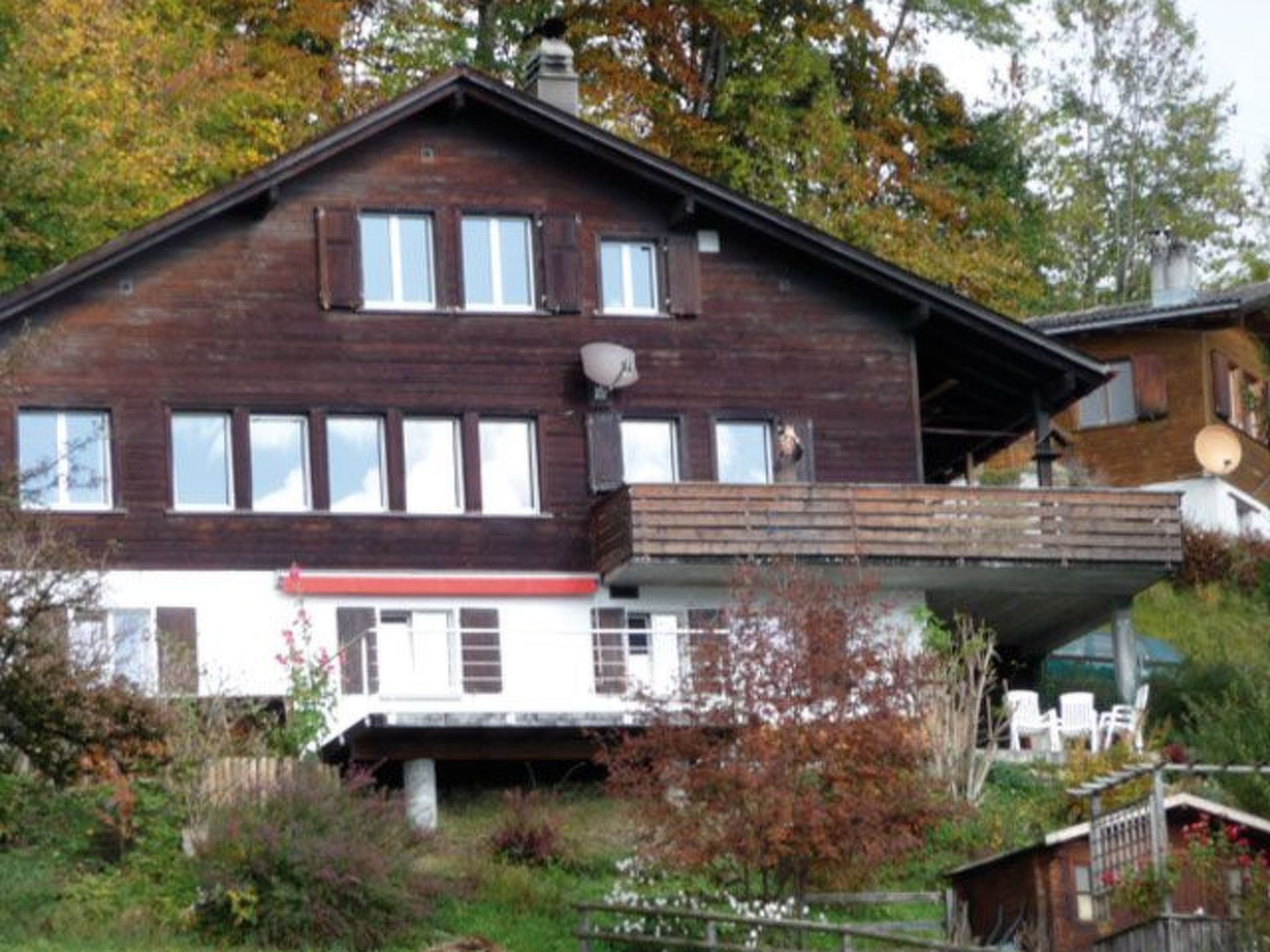 Ein zweistöckiges Holzhaus mit Balkon, umgeben von Bäumen und Vegetation.