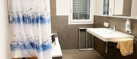 Un baño con cortina de ducha, lavamanos, espejo y ventana.