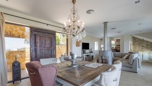 A dining area with a wooden table, chairs, a chandelier, and a stone wall. - Villa with Pool and Spectacular Sea Views (Sa Riera)