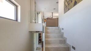 A staircase with beige steps leading to a second-floor area, a glass railing, and a wall-mounted artwork. - Villa with Pool and Spectacular Sea Views (Sa Riera)