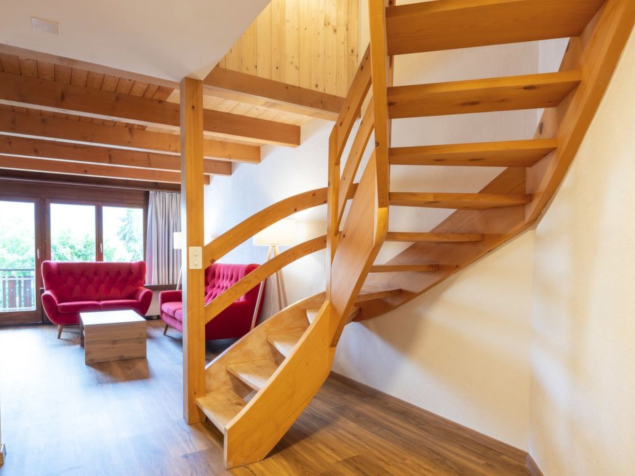 Eine Holztreppe mit modernem Interieur, ein rotes Sofa und ein Holztisch.