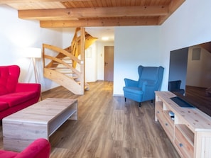 A modern living room with a wooden staircase, a red sofa, a blue armchair, and a wooden coffee table.