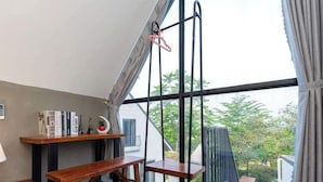 Ein Zimmer mit einem großen Fenster, einem hölzernen Regal mit Büchern, einer Lampe und einem roten Gegenstand auf dem Regal.