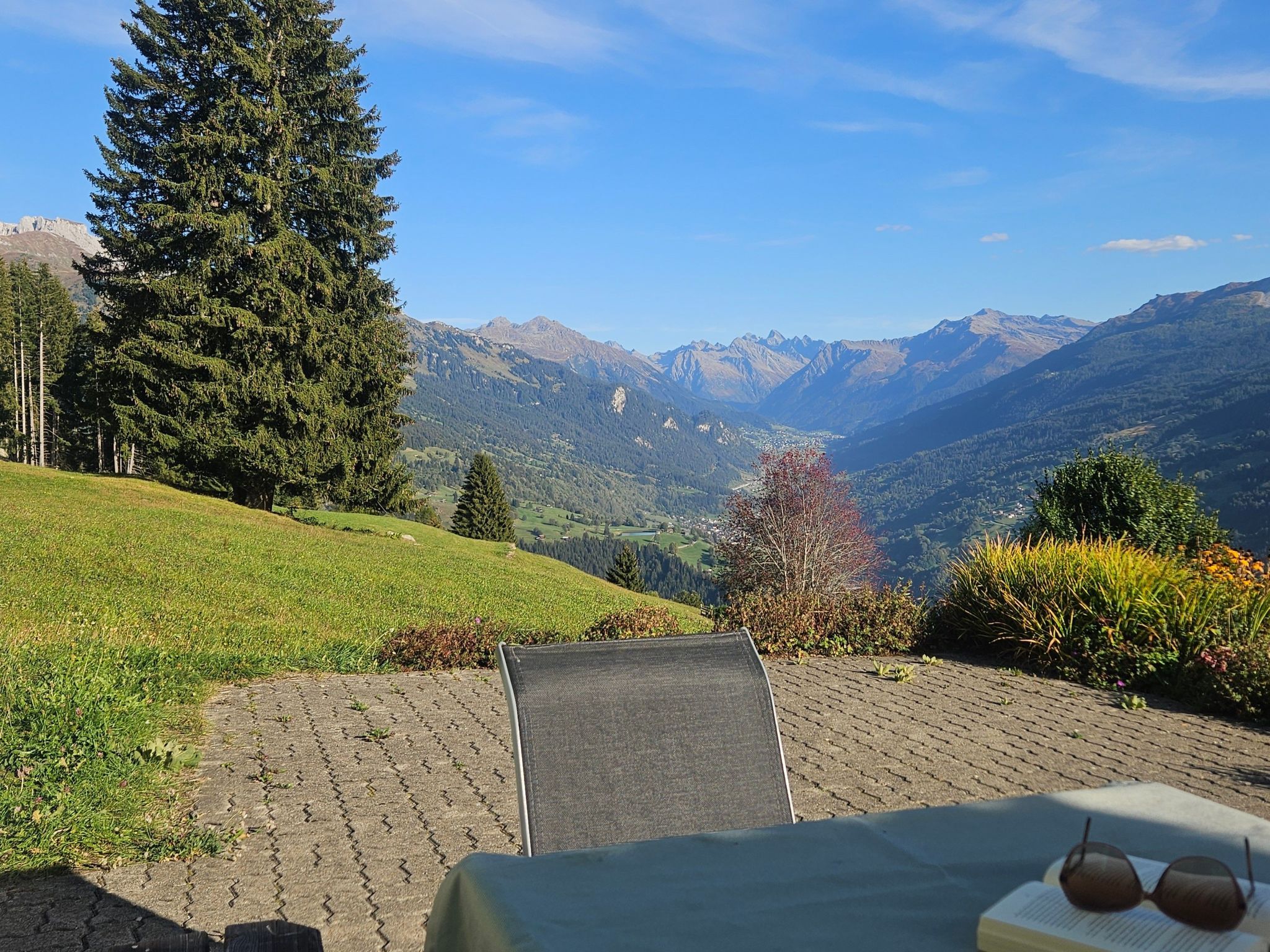 A terrace with a view of mountains, a chair, and a table with sunglasses on it.