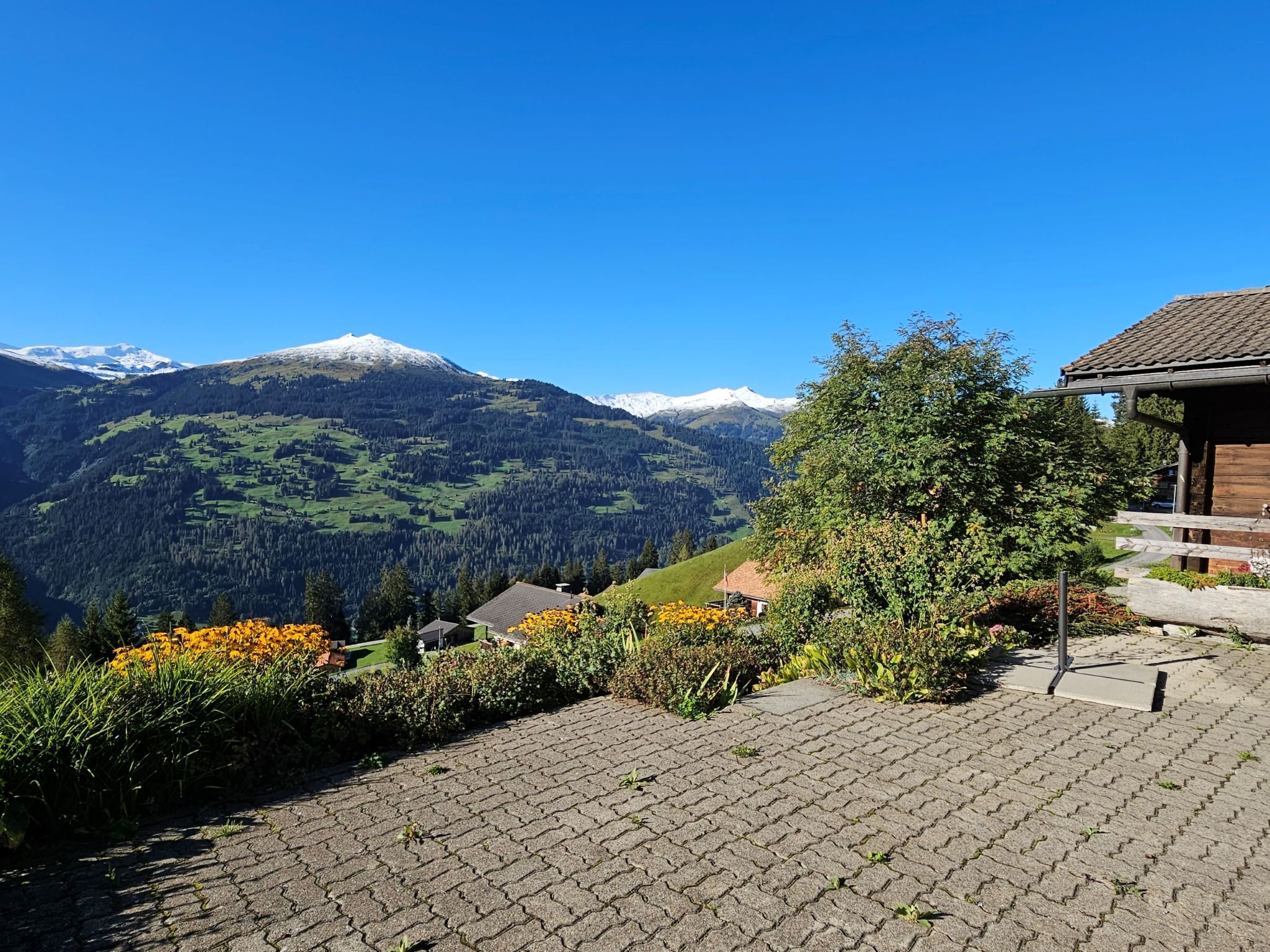 Un sentier pavé mène à un bâtiment en bois d’où l’on peut admirer des montagnes aux sommets enneigés.