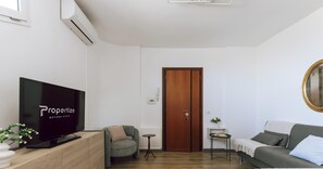 A modern living room with a flat-screen TV, a wooden door, a green armchair, a small round table, and a grey sofa. - Michi’s Attic by Propertize (Cagliari)
