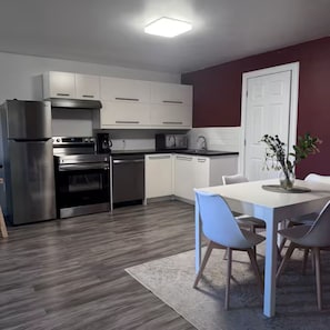 A modern kitchen with stainless steel appliances, white cabinetry, and a dining area with a white table and chairs. - Newly Renovated Bedford Suite (Halifax)