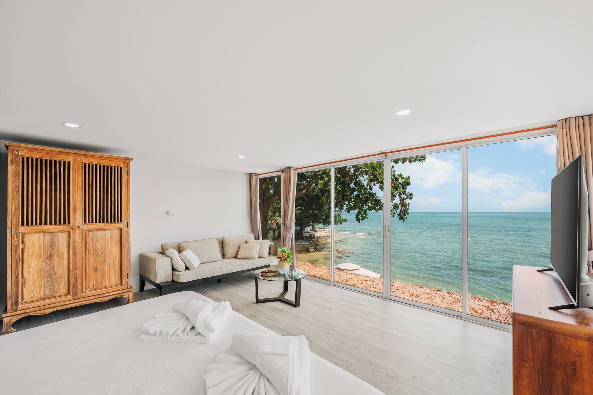 Een slaapkamer met een groot bed, een houten garderobe, een bank, een televisie en uitzicht op zee.
