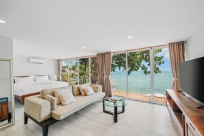 A bedroom with a bed, sofa, TV, and a large window with a beach view. - Room-escape Beach Front Cottage - 2 bed (Koh Samui)