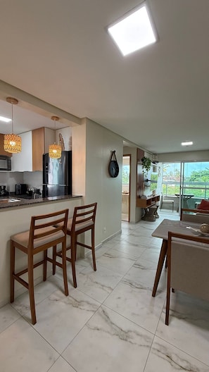 A spacious kitchen with a dining area, marble flooring, and a view of greenery outside. - TNP - Makaranduba 301 (Ipojuca)