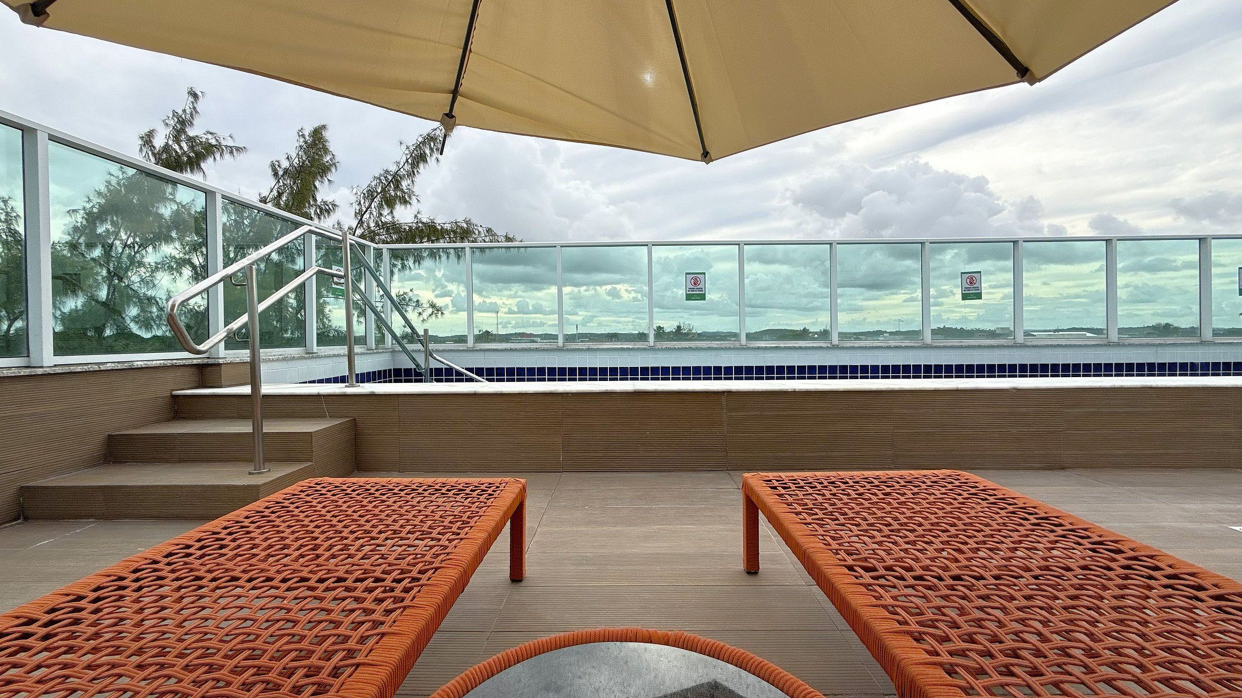 A poolside area with wicker lounge chairs, a glass balustrade, and a view of the pool.